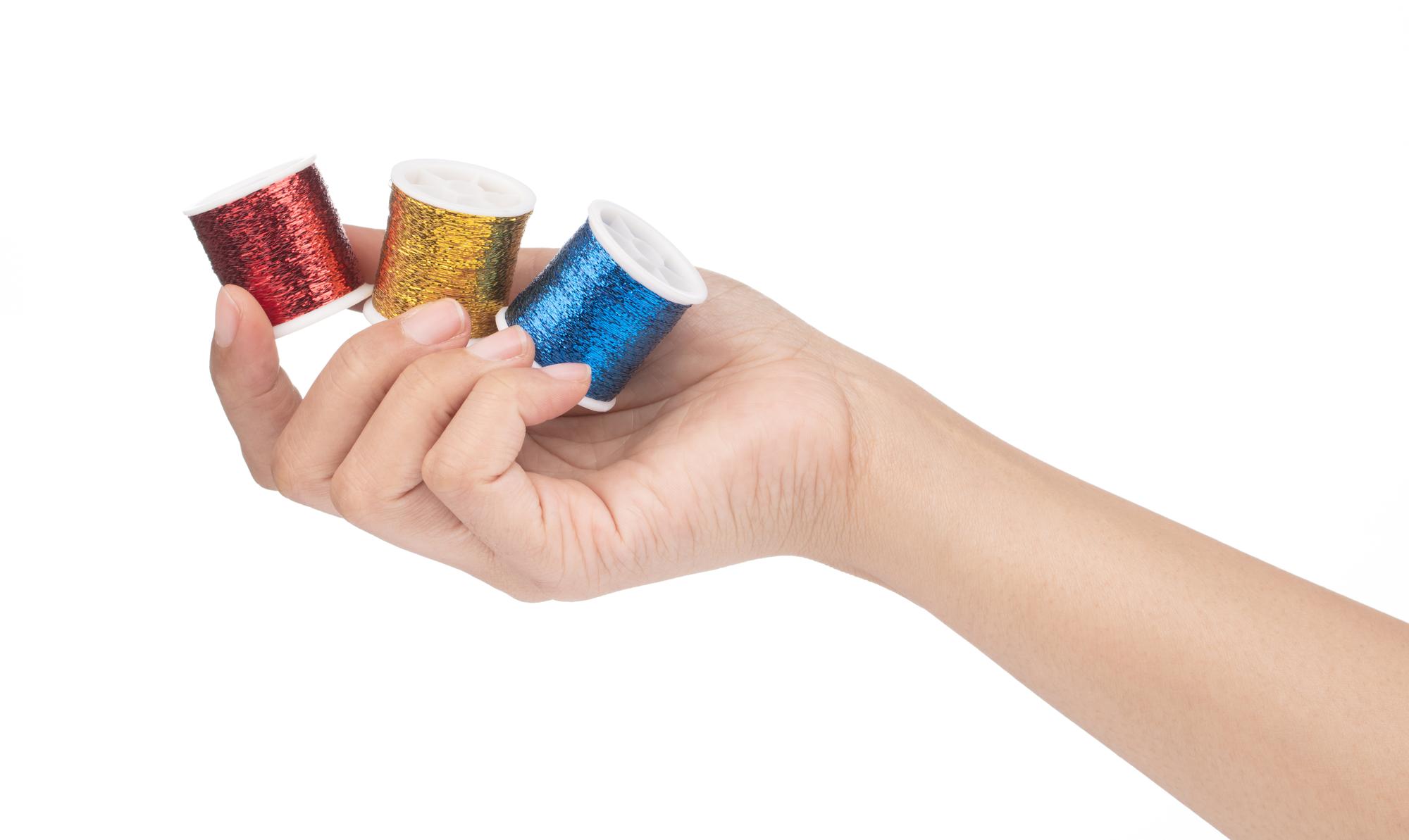 Hands holding embroidered sample next to thread spools